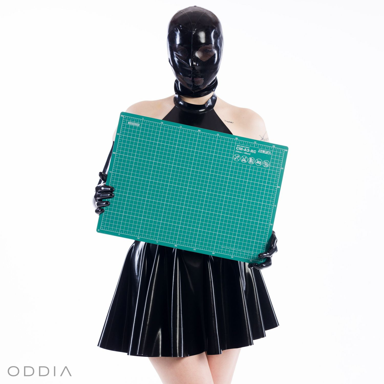 Girl in latex clothing holding a green cutting mat on latex